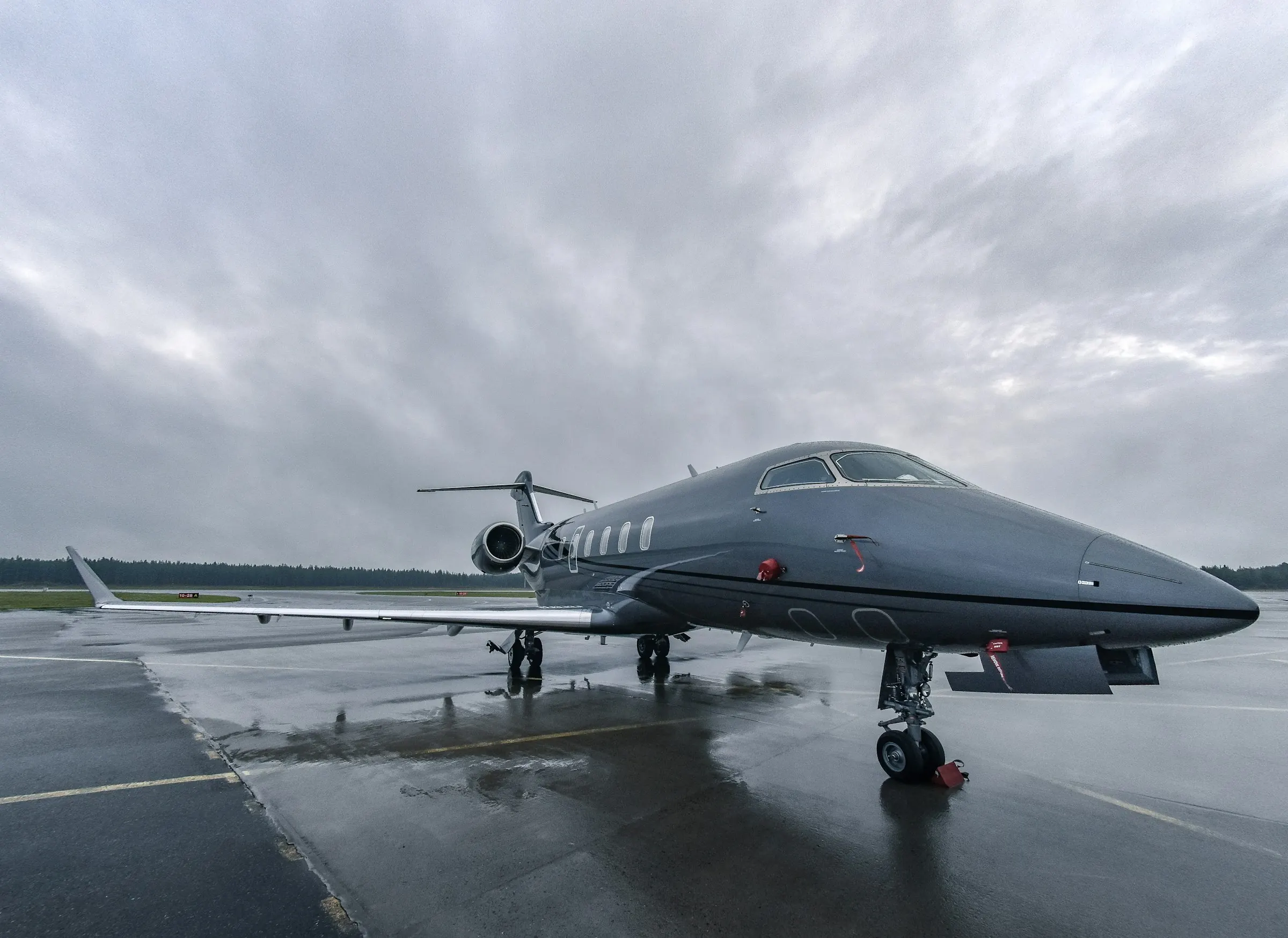 A dark business jet on a rain-soaked ramp under a low grey sky